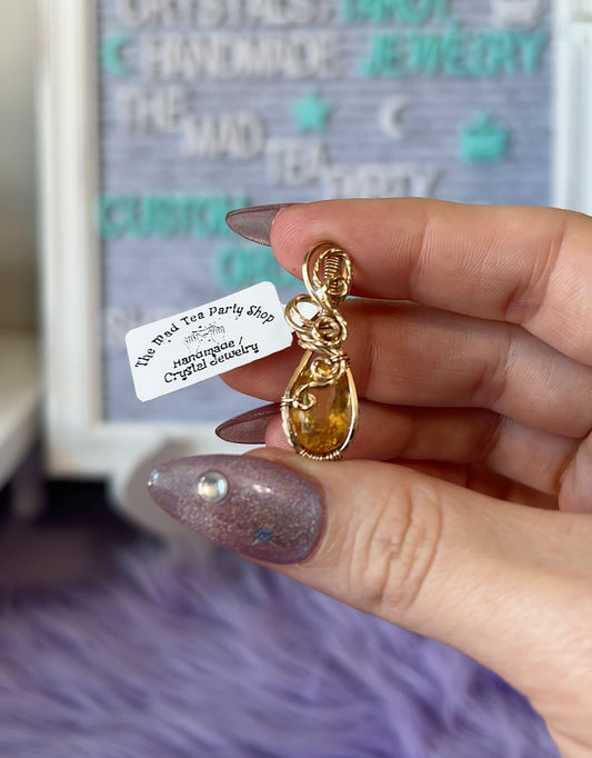 Gold teardrop-shaped pendant with a gemstone held by a hand against a blurred background.
