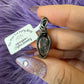 Hand holding a silver pendant with a tag from The Tea Party Shop on a purple fluffy background