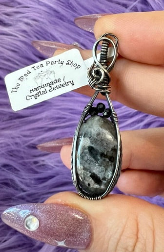 Handmade larvikite pendant wrapped in oxidized silver with hematite beads, held in hand on purple fur background
